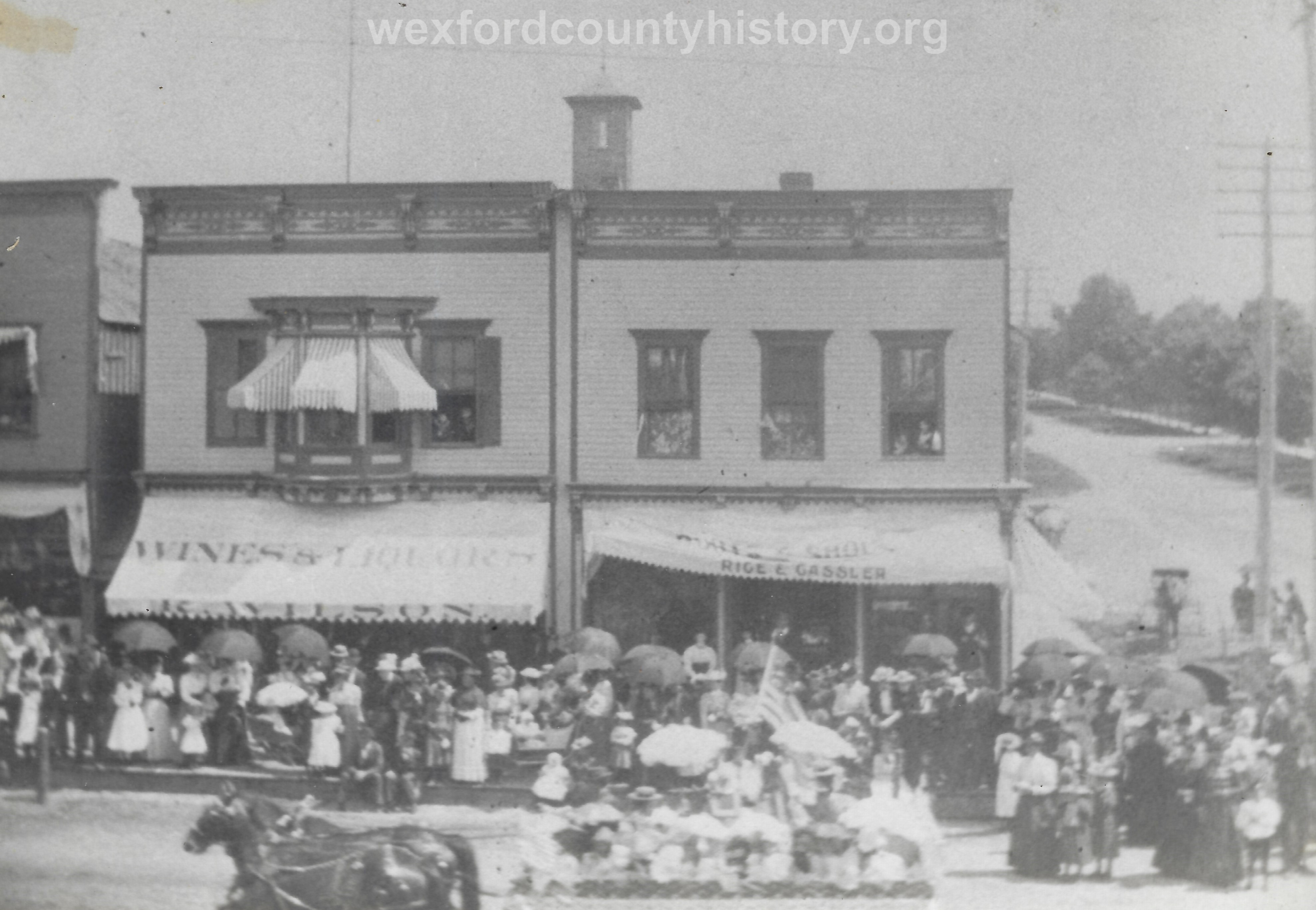 Cadillac-Parade-Early-1900s-parade-On-The-Corner-Of-Cass-And-South-Mitchell-Wilsons-Saloon-and-the-Rice-And-Cassler-Business-are-in-the-background